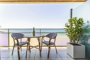 Een balkon met twee rieten stoelen en een tafel, een bloempot en uitzicht op zee.