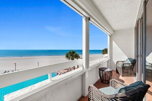 Ein Balkon mit Blick auf Strand und Pool, mit Korbmöbeln und einer weißen Wand.