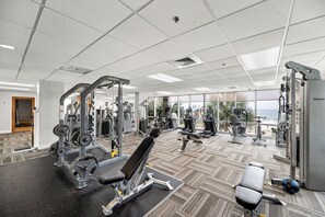 Ein Fitnessstudio mit unterschiedlichen Trainingsgeräten, großen Fenstern und Blick auf den Ozean.