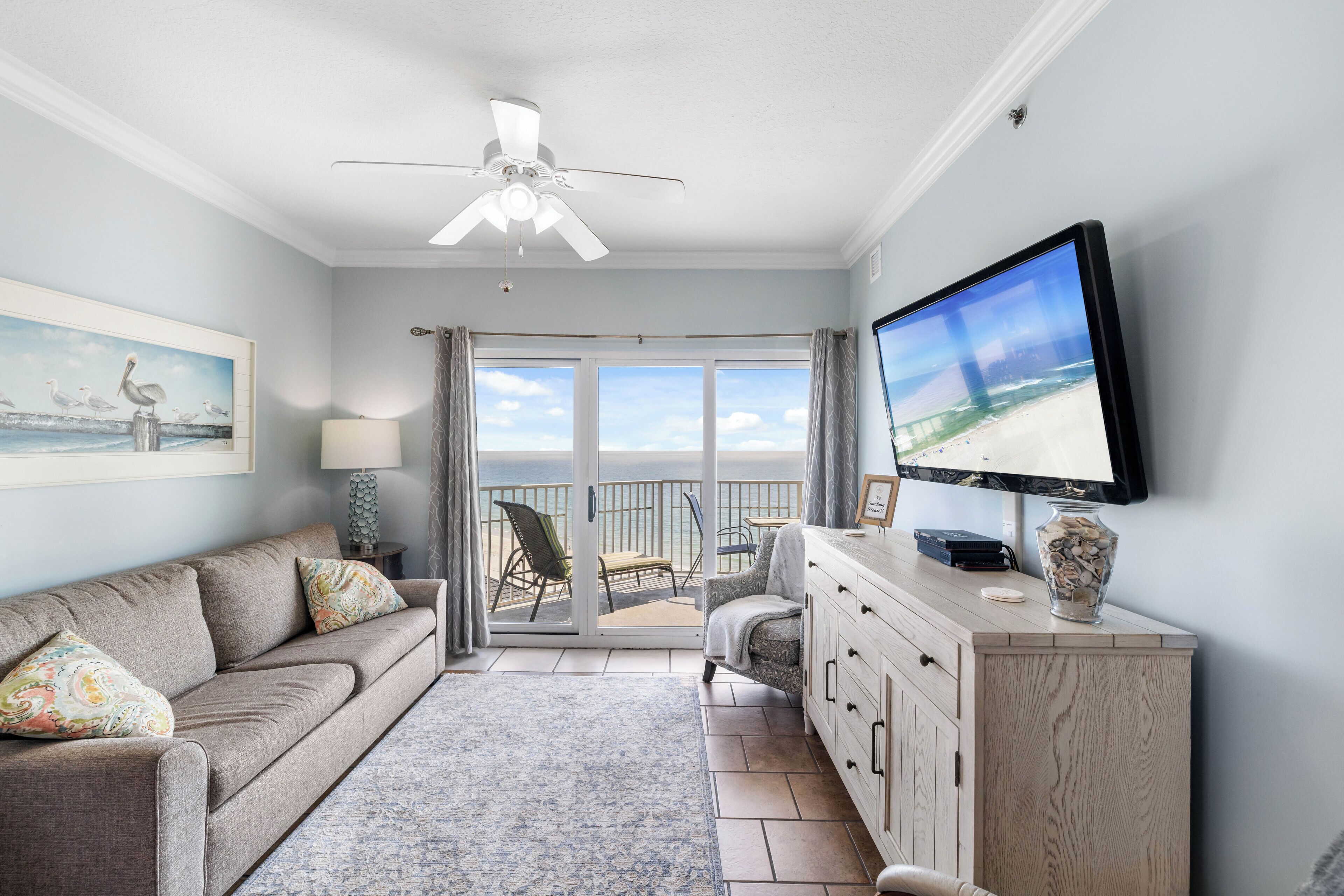 A living room with a sofa, TV, and a view of the ocean through a sliding glass door.
