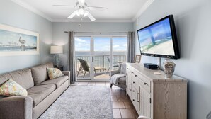 Ein Wohnzimmer mit Sofa, Fernseher und Meerblick durch eine Glastür.