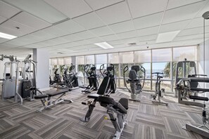 A gym with various exercise machines, large windows, and a carpeted floor. - Seawind 1001 by Liquid Life (Gulf Shores)