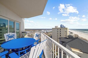 Ein Balkon mit Tisch und Stühlen mit Blick auf einen Strand und Gebäude.