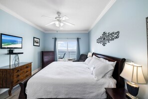 Ein Schlafzimmer mit Bett, Fernseher, Schminktisch, Stuhl, Lampe und einem Balkon mit Blick.
