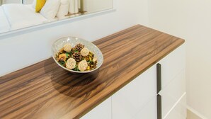 Een moderne hotelkamer met een houten nachtkastje, een schaal decoratieve objecten, een bed met witte lakens en een grote spiegel die de kamer reflecteert.