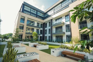 A modern multi-story building with a courtyard featuring planters, benches, and a grassy area. - Spacious One Bedroom at Embassy Gardens (Accra)