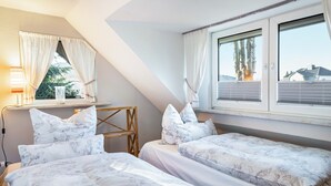 Ett sovrum med två sängar, ett skrivbord och ett fönster med gardiner.