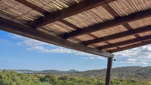 A covered outdoor seating area with a sofa and a table, overlooking a landscape with trees and hills. - Romantic Suite Apt.21 - Olbia (Olbia)