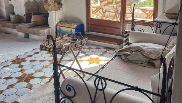 A cozy bedroom with a large arched window, a rustic stone fireplace, a metal bed frame, and a tiled floor. - Romantic Suite Apt.21 - Olbia (Olbia)