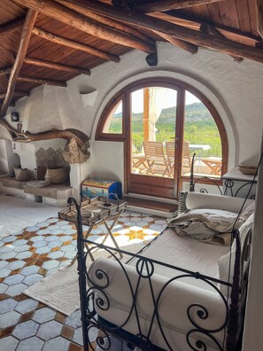 Um quarto acolhedor com uma grande janela em arco, uma lareira de pedra rústica, estrutura de cama de metal e chão revestido de azulejos.