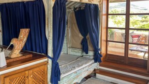 A rustic wooden room with a four-poster bed, blue curtains, and a view of greenery outside. - Romantic Suite Apt.21 - Olbia (Olbia)