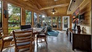 Un intérieur en bois comprenant une table à manger, des chaises, un ventilateur de plafond et de grandes fenêtres.
