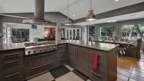 Une cuisine moderne dotée d’un grand îlot central, d’appareils électroménagers en acier inoxydable et de luminaires suspendus.