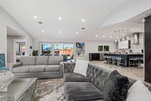 A modern living room with a grey sofa, a tufted armchair, and a dining area with a bar.