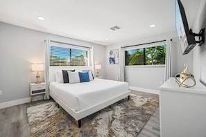 A modern bedroom with a large bed, bedside tables, a TV, and a view of greenery.
