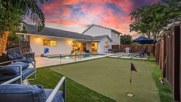 A backyard with a swimming pool, artificial grass, and a patio area with outdoor furniture. - Heated Pool - Putting Green - 5 min From Beach! (Deerfield Beach)