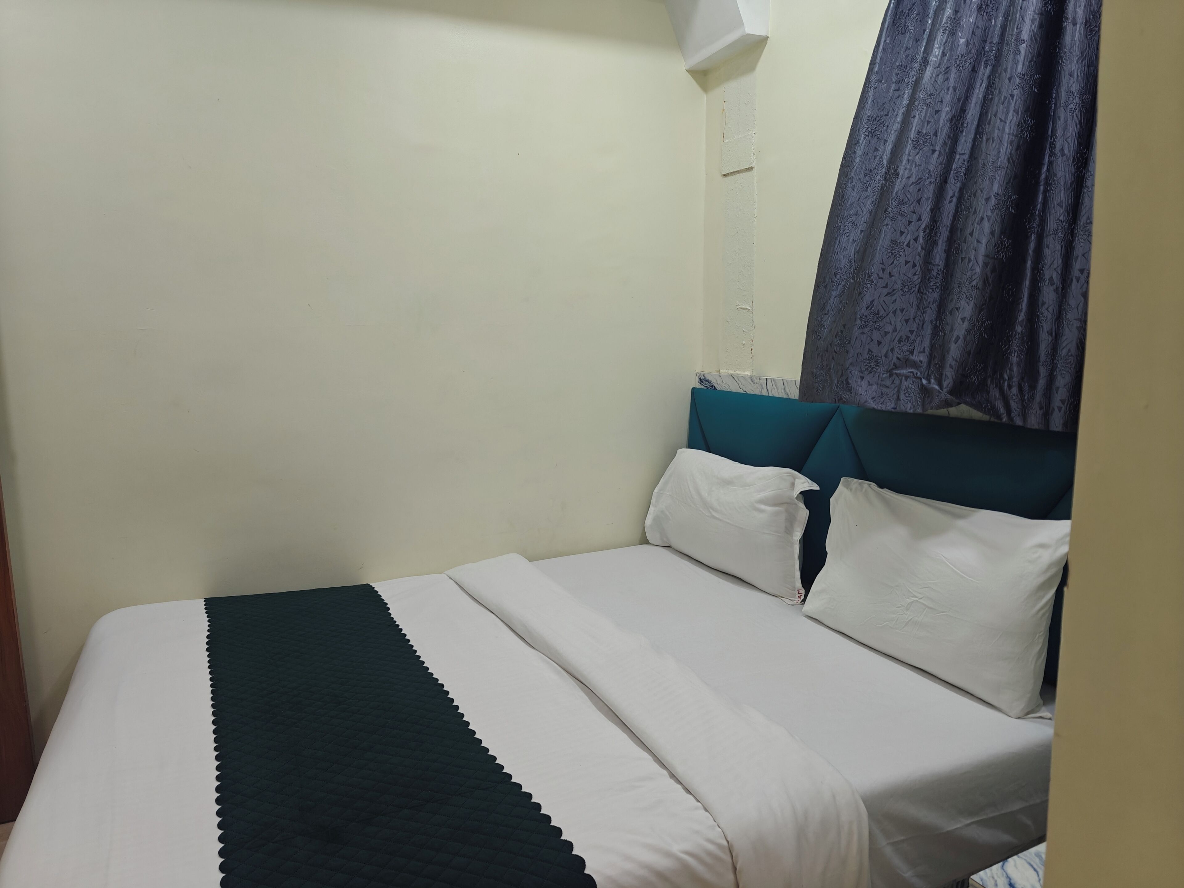 A bed with white and teal bedding, a headboard, and a curtain.