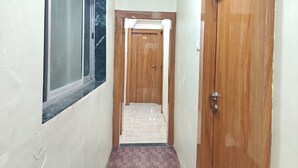 A narrow hallway with a window on the left, a wooden door on the right, and a tiled floor. - HOTEL GLOW STAR (Mumbai)