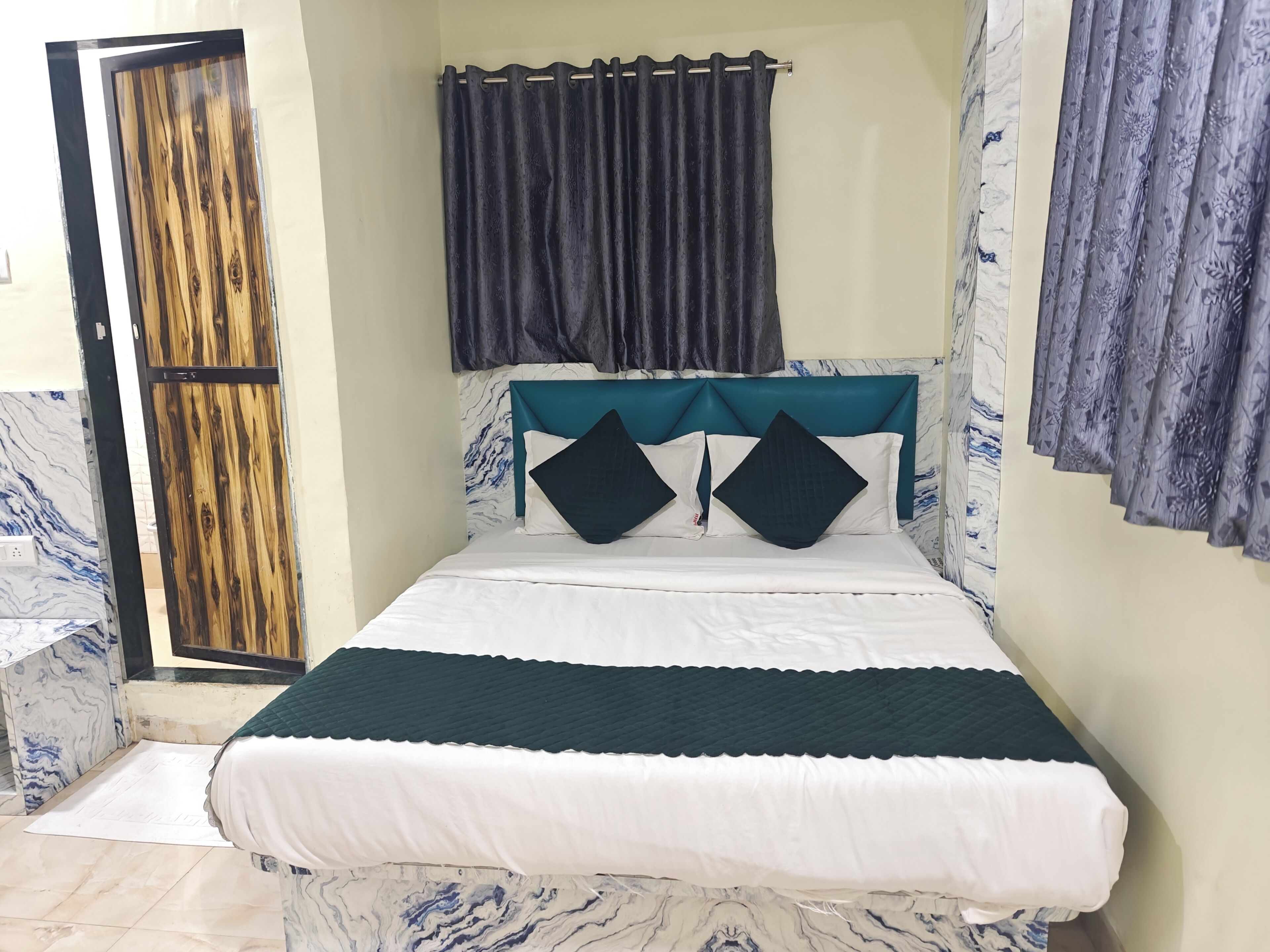 A bedroom with a bed, a wooden door, a curtain, and a marble-patterned wall.