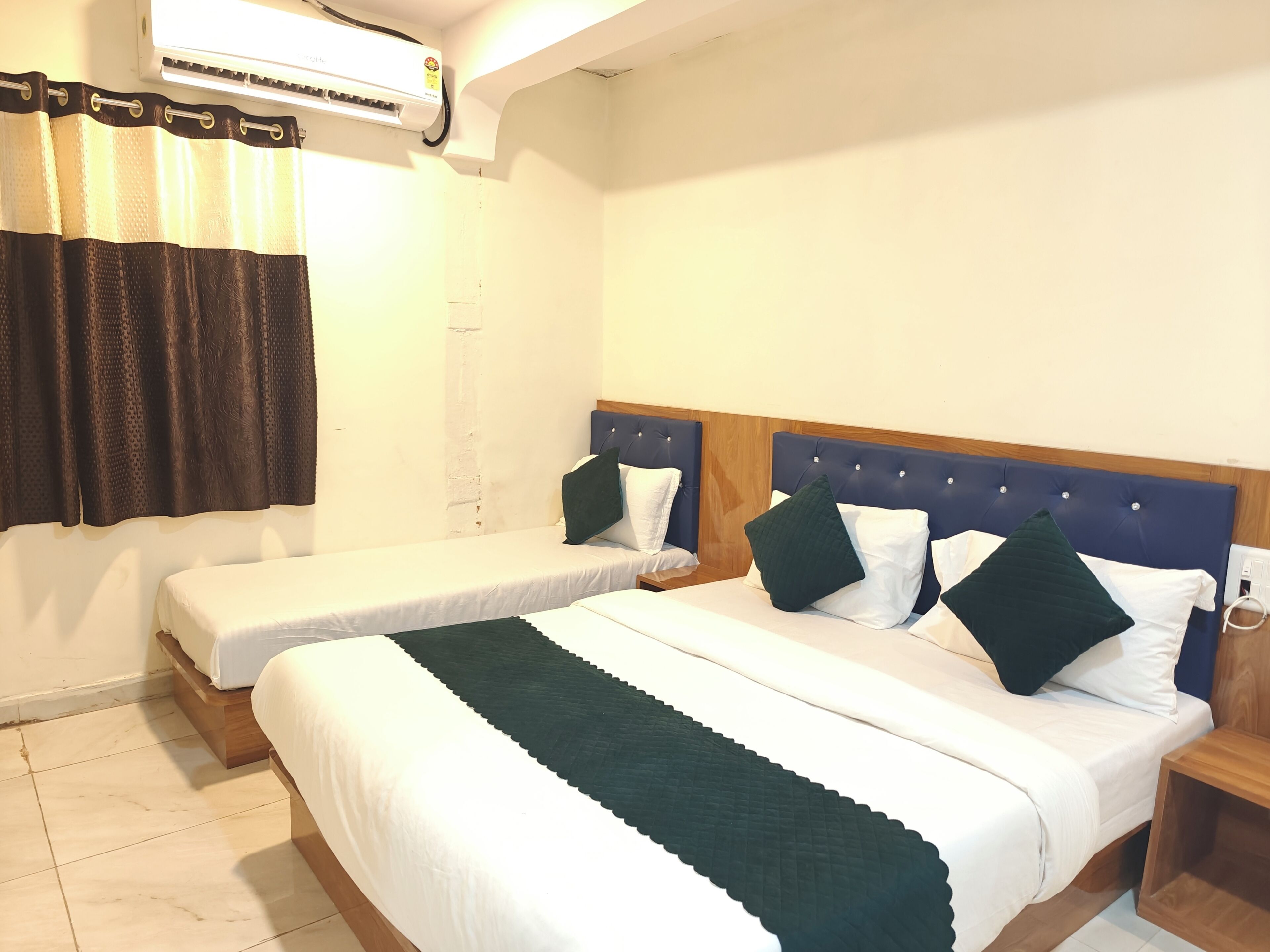 Une chambre d’hôtel avec deux lits simples, une tête de lit en bois, un climatiseur blanc et un rideau.
