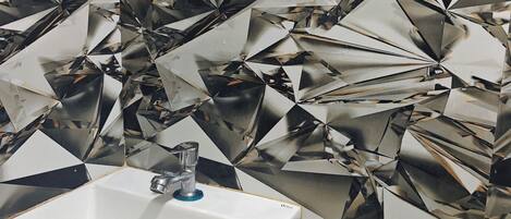 A bathroom with a sink, a mirror, and a wall with a geometric tile pattern.