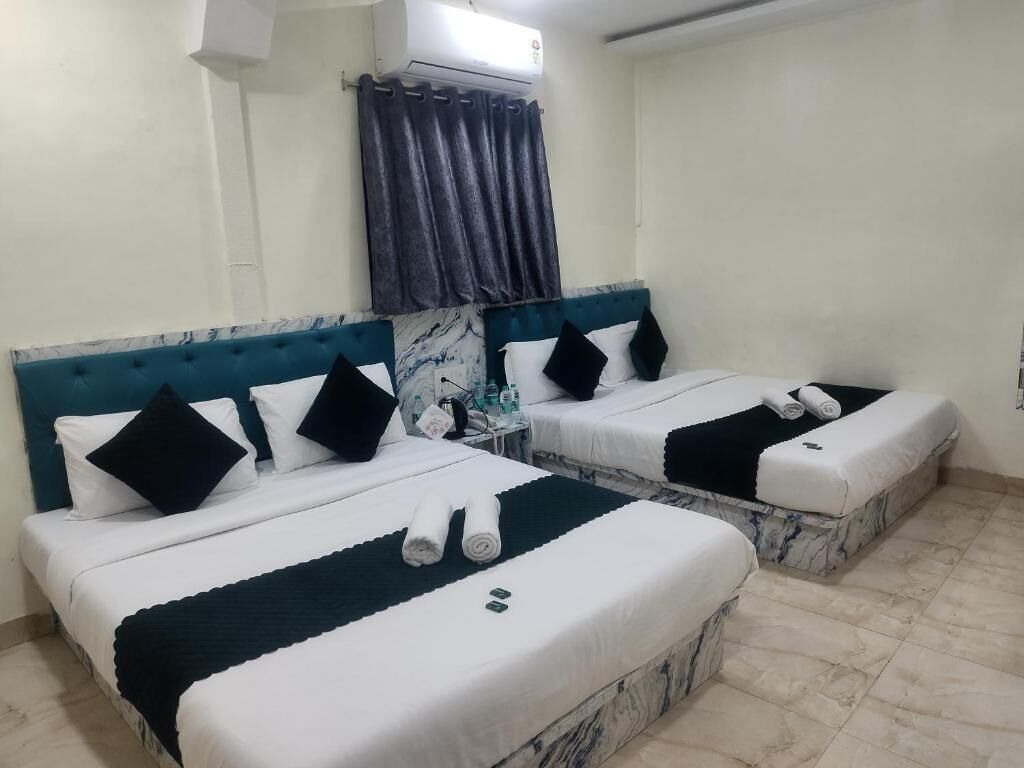 A hotel room with two beds, each with white bedding and black pillows. There is a marble headboard, a small table with toiletries, and an air conditioning unit on the wall.