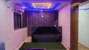 A reception area with a black reception desk, patterned wallpaper, a clock, and a ceiling with blue lighting. - HOTEL GLOW STAR (Mumbai)