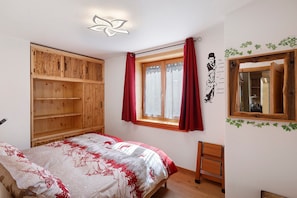 A bedroom with a bed, wooden wardrobe, window with curtains, mirror, and wall decorations. - Apartment '3' with Lake View, Shared Garden and Wi-Fi (Livigno)