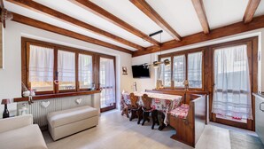 Una habitación acogedora con vigas de madera, una mesa de comedor con sillas, un sofá y un televisor colgado en la pared.