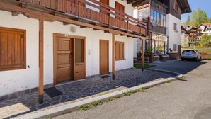 Un edificio con balcones de madera, suelo empedrado de piedra y un coche estacionado frente a él.