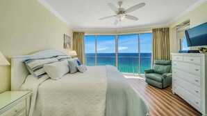 A hotel room with a large bed, a ceiling fan, a green chair, a TV, and a view of the ocean. - Relax & Recharge in This 19th-Floor Getaway (Panama City Beach)