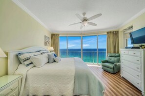 Ein Hotelzimmer mit einem großen Bett, einem Deckenventilator, einem grünen Sessel, einem Fernseher und Meerblick.