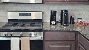 Una cocina con estufa de acero inoxidable, microondas, armarios de madera oscura, cafetera y tostadora.