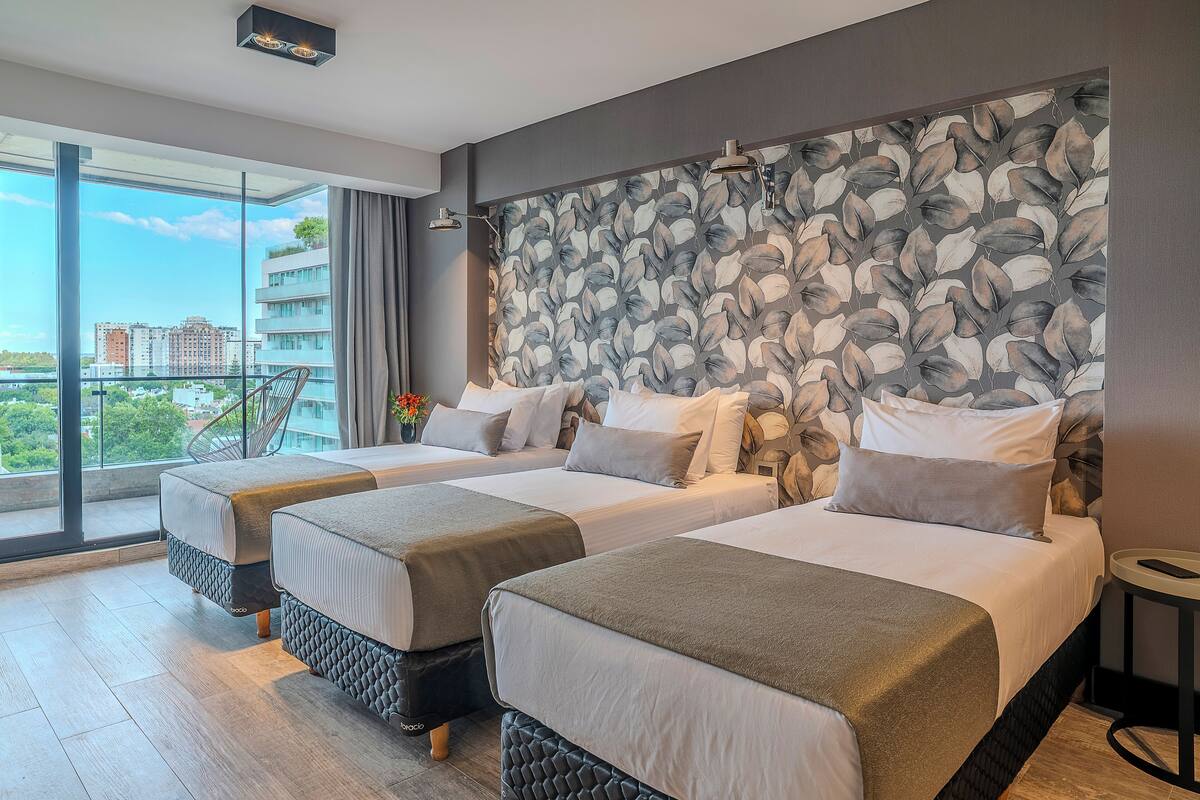 Hotelkamer met twee bedden, een balkon met uitzicht op de stad en een behang met patroon.