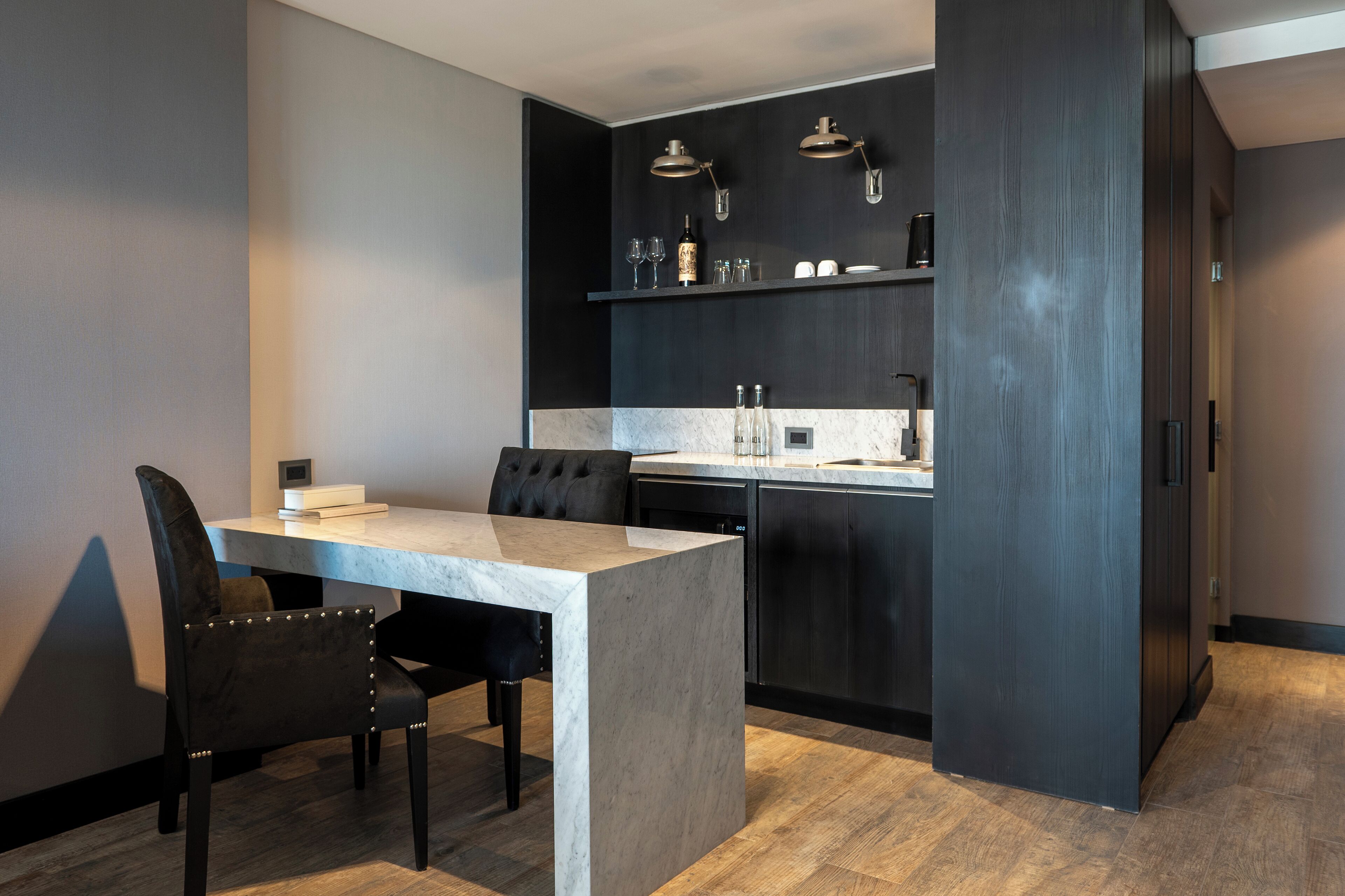 A modern kitchen with dark cabinetry, a marble countertop, and a dining area with a table and chairs.