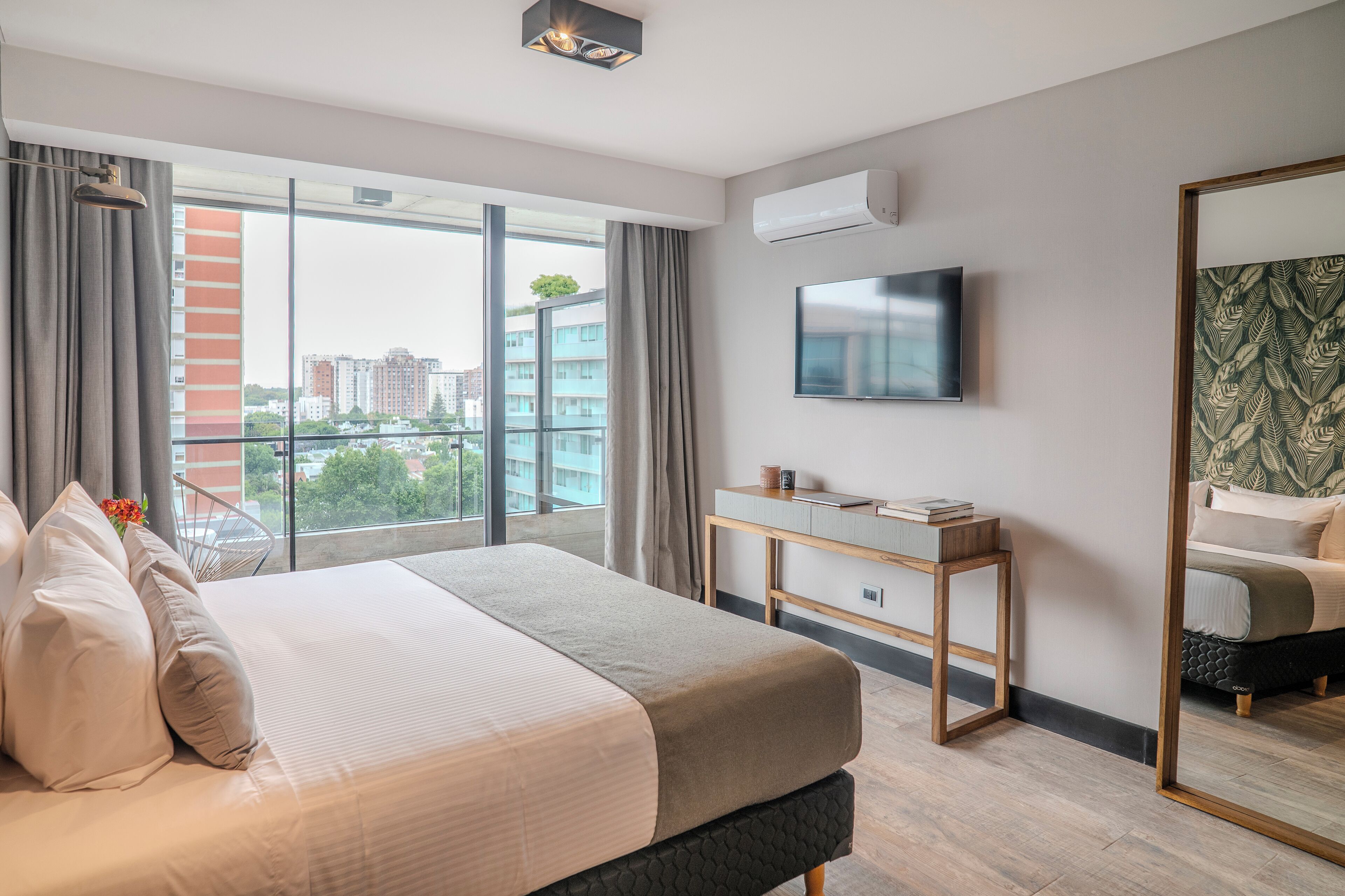 Habitación de hotel moderna con una cama grande, un escritorio, un televisor y un ventanal que ofrece vistas a la ciudad.