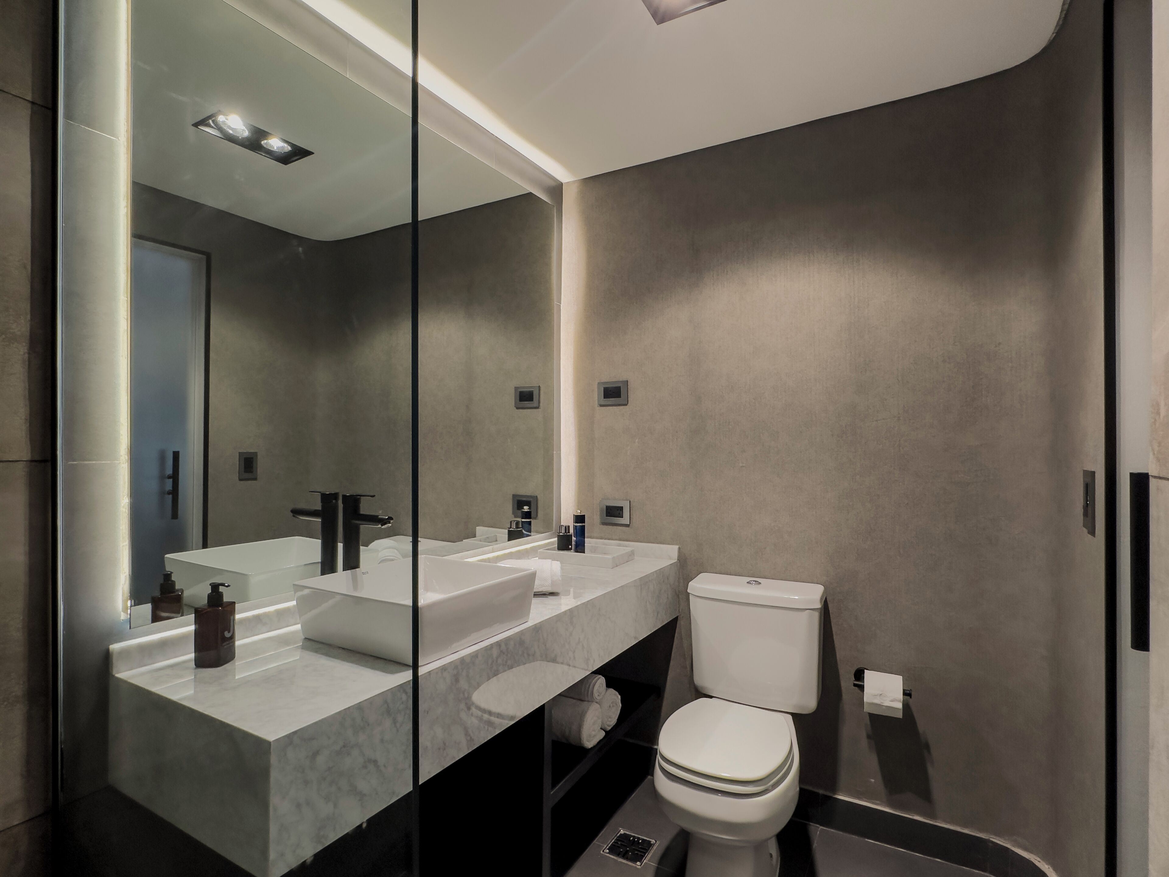 Un baño moderno con un espejo grande, dos lavamanos, un inodoro y una zona de ducha.