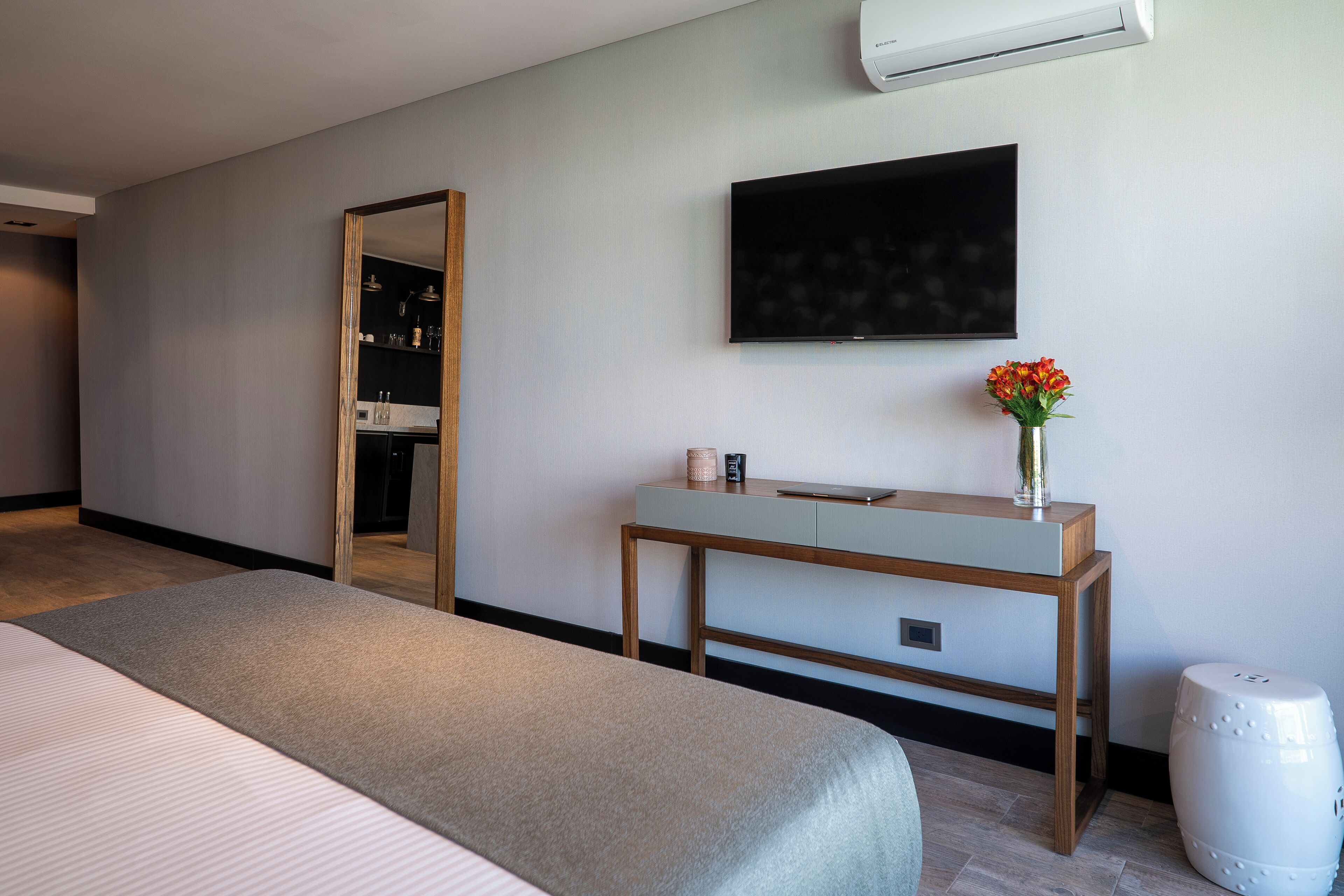 Une chambre d’hôtel moderne, équipée d’un lit, d’une table de chevet agrémentée d’un vase de fleurs, d’un téléviseur à écran plat et d’un miroir.