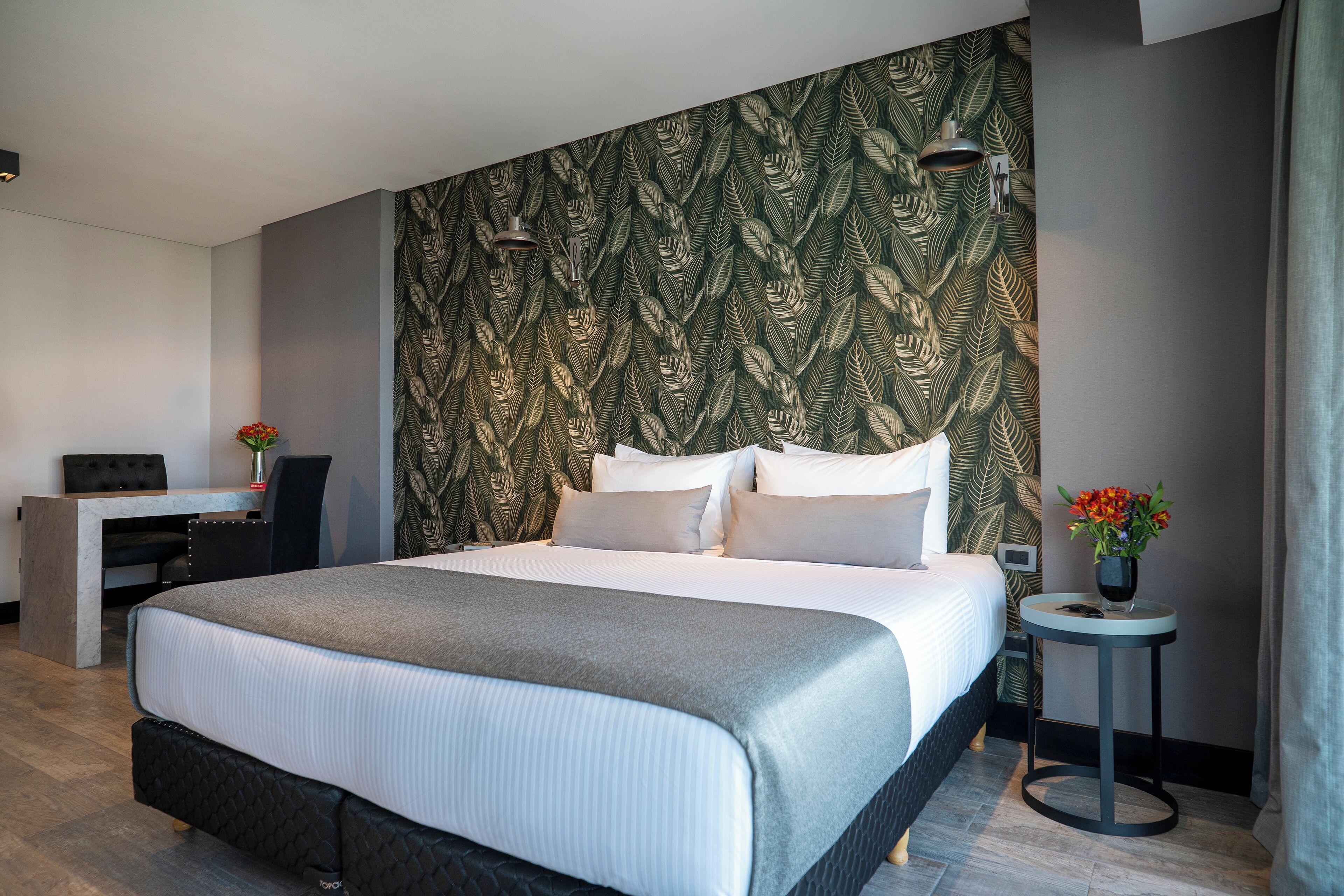 A modern hotel room with a large bed, a desk, and a small table with flowers.