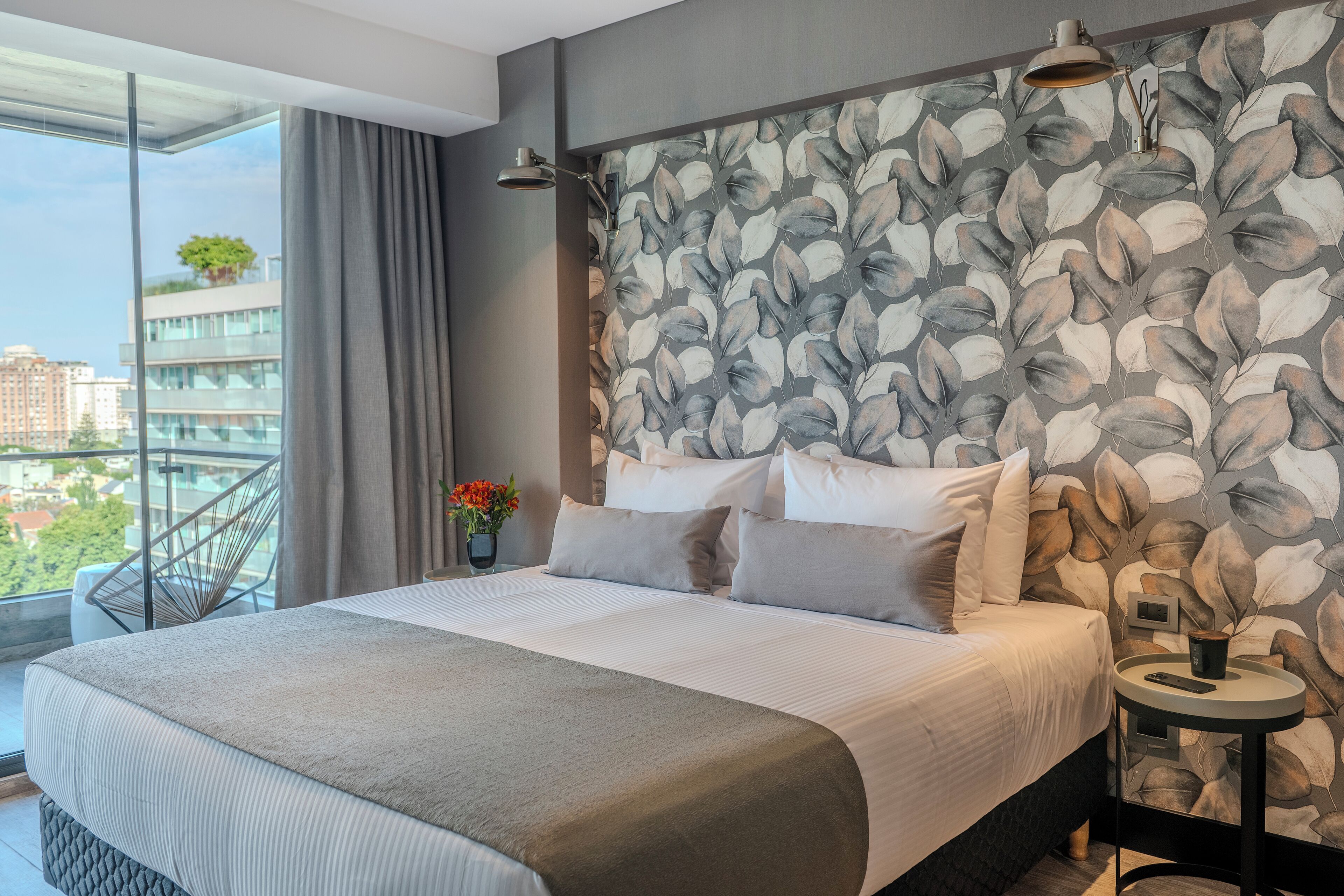 Una habitación de hotel moderna con una cama grande, vista a la ciudad y una pared decorada con motivos de hojas.