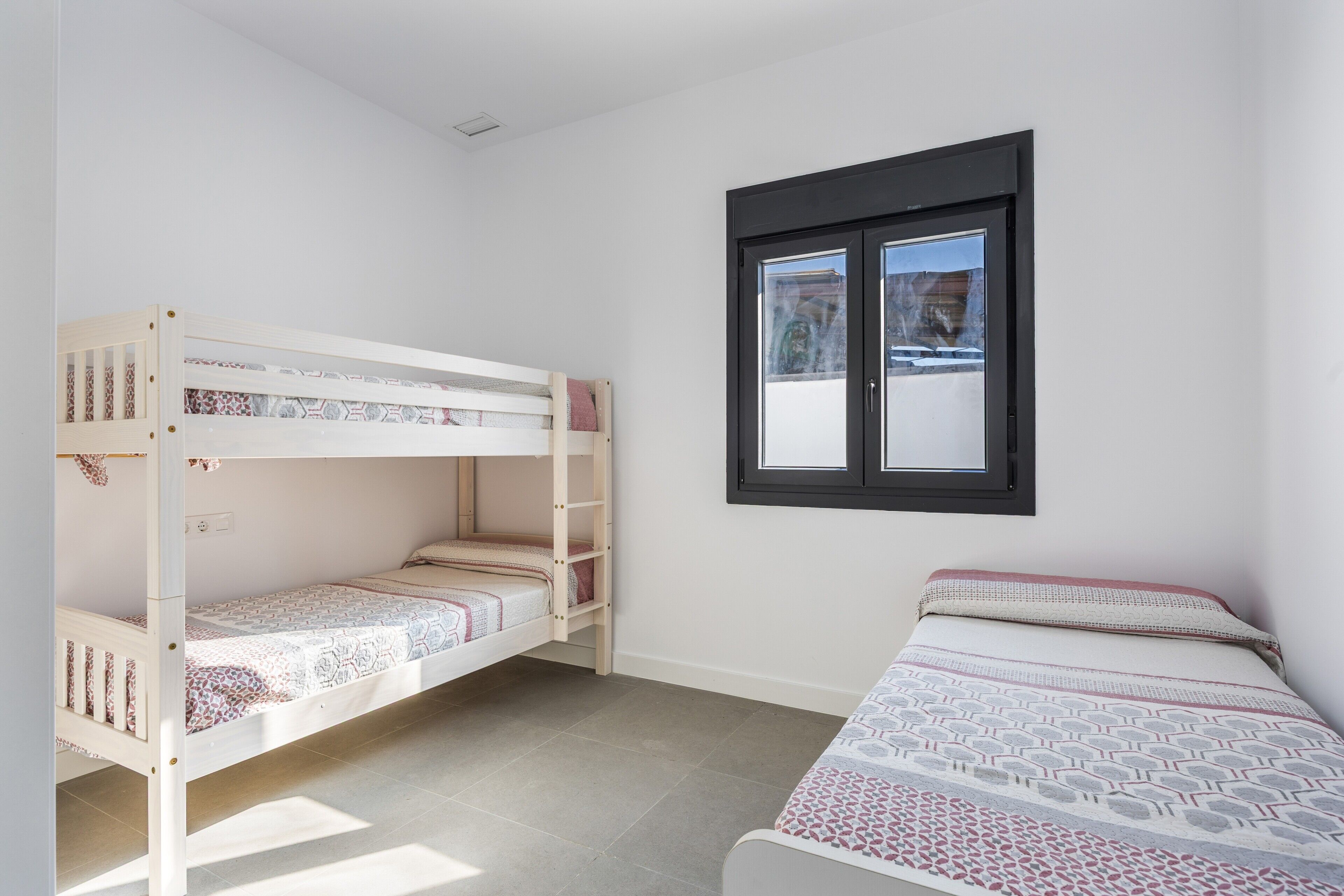 Une chambre avec un lit superposé, un lit simple, une fenêtre donnant sur un beau paysage et un sol carrelé.