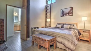 A bedroom with a bed, bedside tables, a ladder, a painting, and a view of the kitchen. - Aspen View Lodge 4 bed/3 ba, Sauna, W/D, Views (Brian Head)