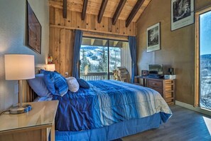 Un dormitorio con cama, un escritorio con una computadora portátil, una lámpara y vista a un paisaje nevado.