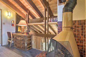 Un interior rústico con un escritorio de madera, una lámpara, una chimenea y una escalera.