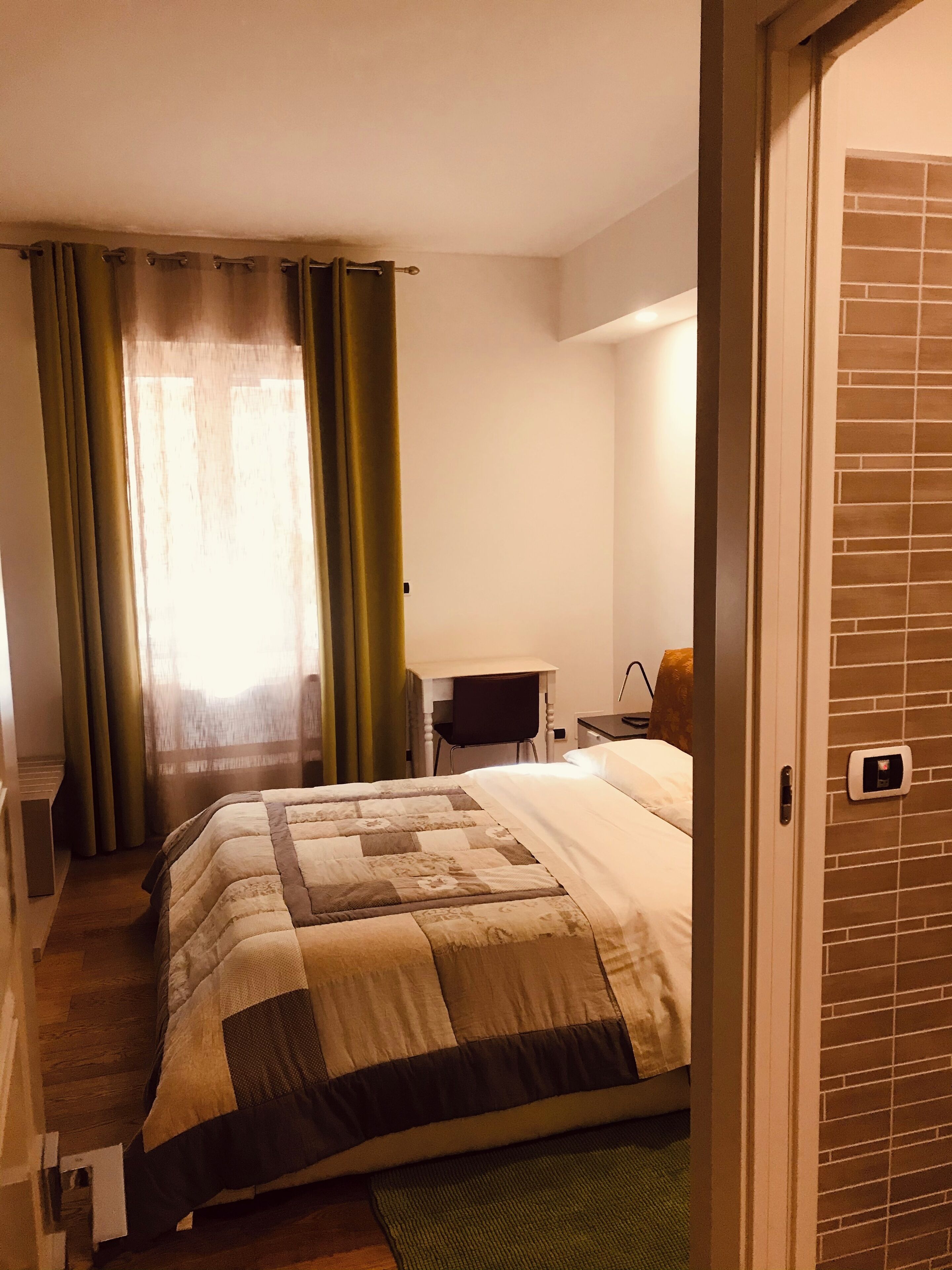 A hotel room with a bed, a desk, a chair, and a window with curtains.
