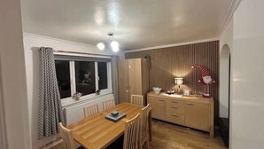 Ein Essbereich mit einem Holztisch und Stühlen, einem Fenster mit Vorhängen, einem Schrank mit einer Lampe und einer gestreiften Wand.