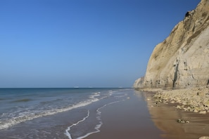 Una playa con un acantilado rocoso y mar tranquilo.