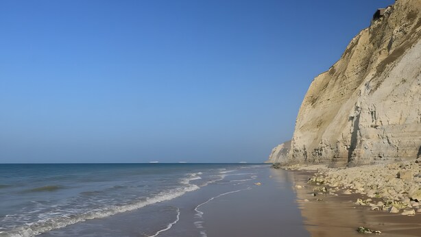 A beach with a rocky cliff and calm sea.