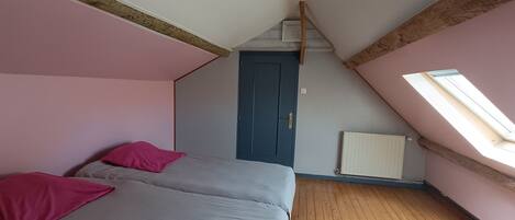 A bedroom with a sloped ceiling, a door, a radiator, and a skylight.
