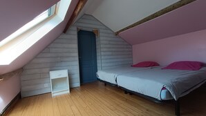 A bedroom with a sloped ceiling, a bed, a small white cabinet, and a door.